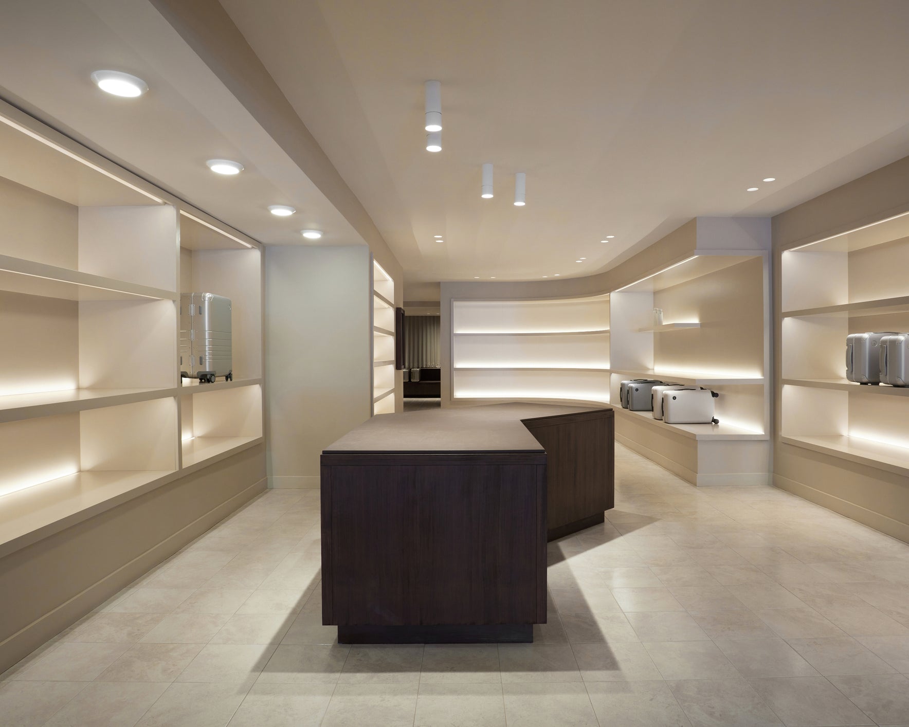 Monos Boston store interior with illuminated shelving and silver luggage displayed in a minimalist space.
