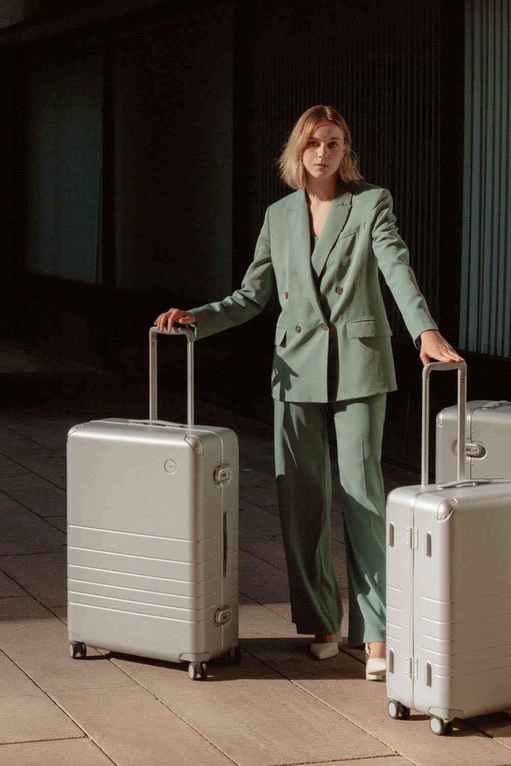 A woman holding a Hybrid Check-In Large, and Medium in Silver. Besides her there is also a Hybrid Trunk, and Carry-On both in Silver.