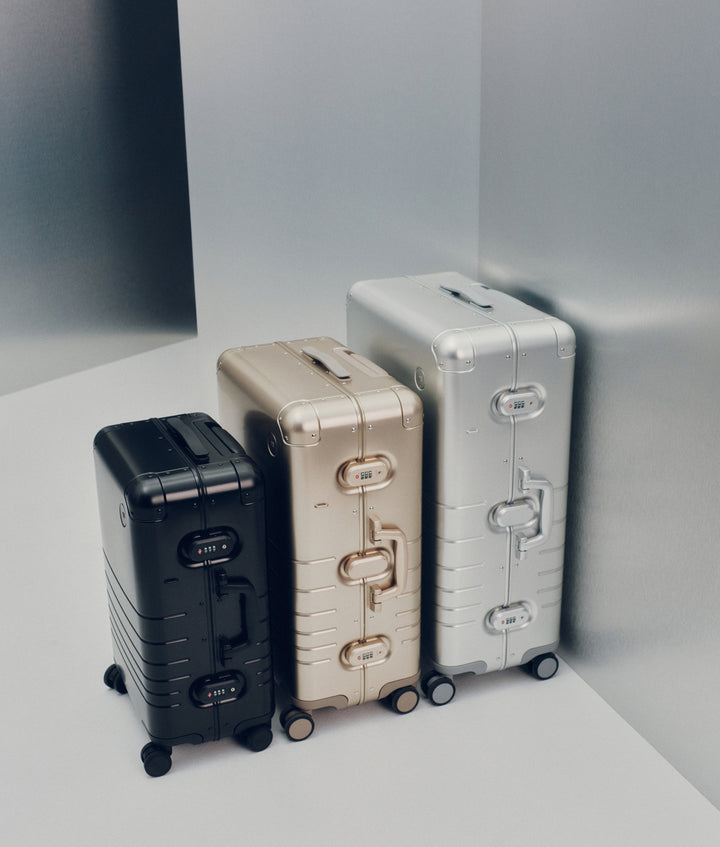 The Monos Aluminum Collection featuring the Carry-On in Caviar Black, Check-In Medium in Champagne Gold, and Check-In Large in Aspen Silver. The sleek aluminum shells and minimalist design highlight Monos’ signature craftsmanship and timeless travel aesthetic.