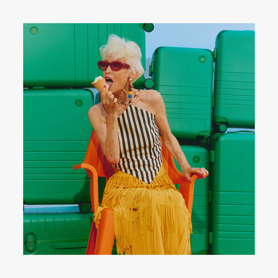 Coastal Blue | Woman eating ice cream in front of a stack of Jungle Green Hybrid suitcases in different sizes