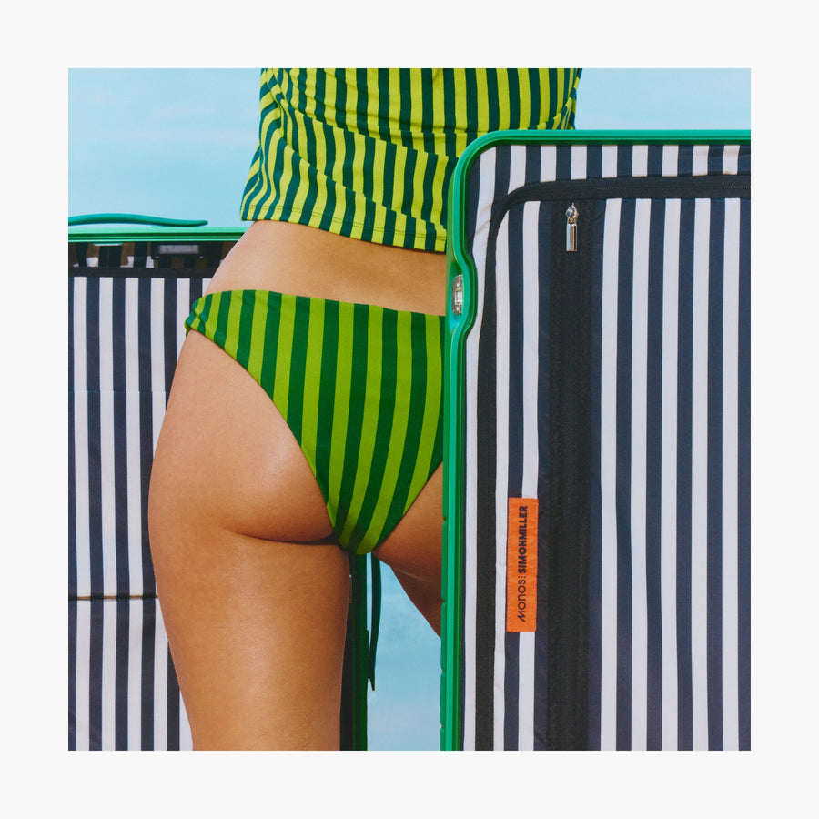 Jungle Green | Close-up of a woman in a green striped swimsuit standing beside an open Jungle Green Hybrid suitcase, revealing its interior Poplin Stripe Black interior