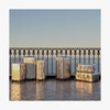 A collection of Monos aluminum suitcases in Aspen Silver in various sizes is arranged on a sunlit terrace with a wrought iron railing, overlooking the ocean in the background. (thumbnail)