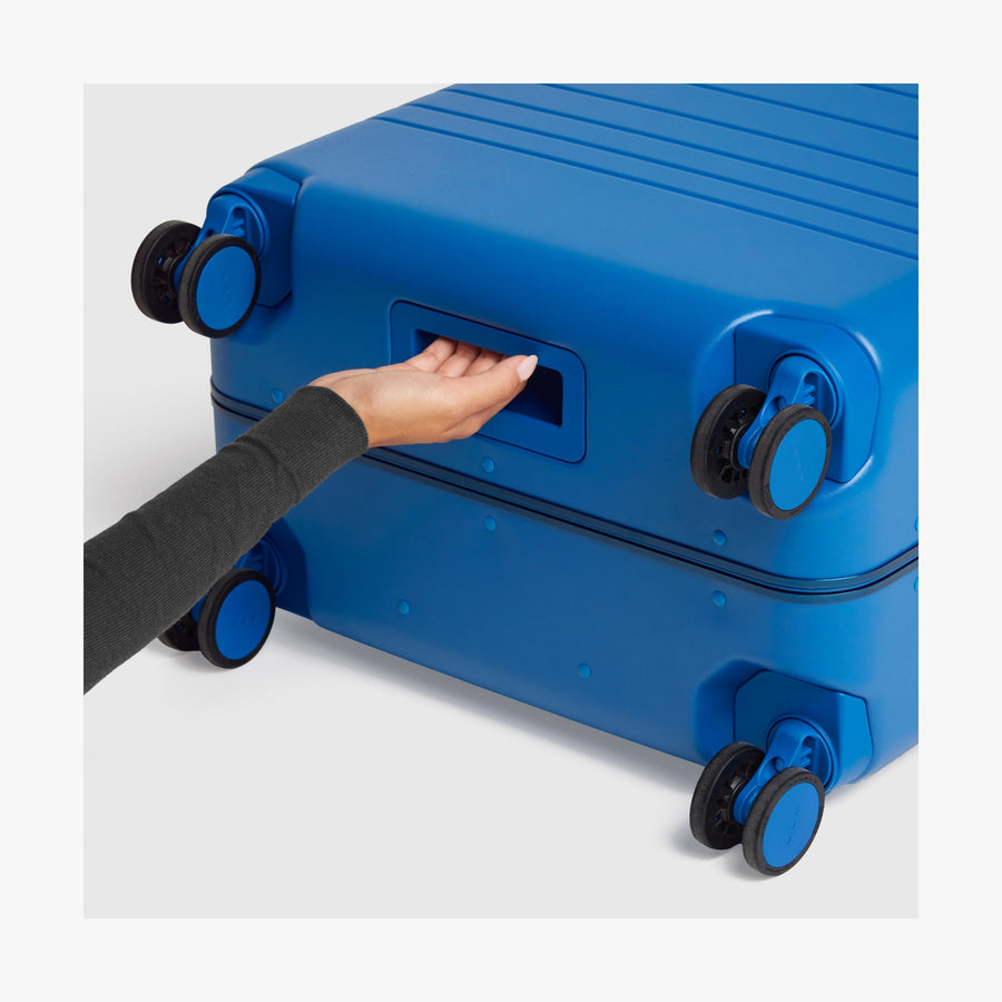 Coastal Blue | Close-up view of a hand gripping the built-in underside handle of a Coastal Blue Hybrid suitcase