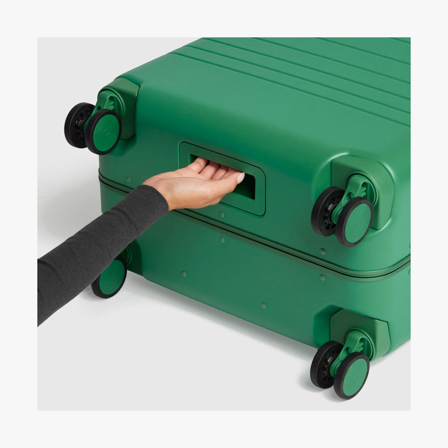 Jungle Green | Close-up view of a hand gripping the built-in underside handle of a Jungle Green Hybrid suitcase