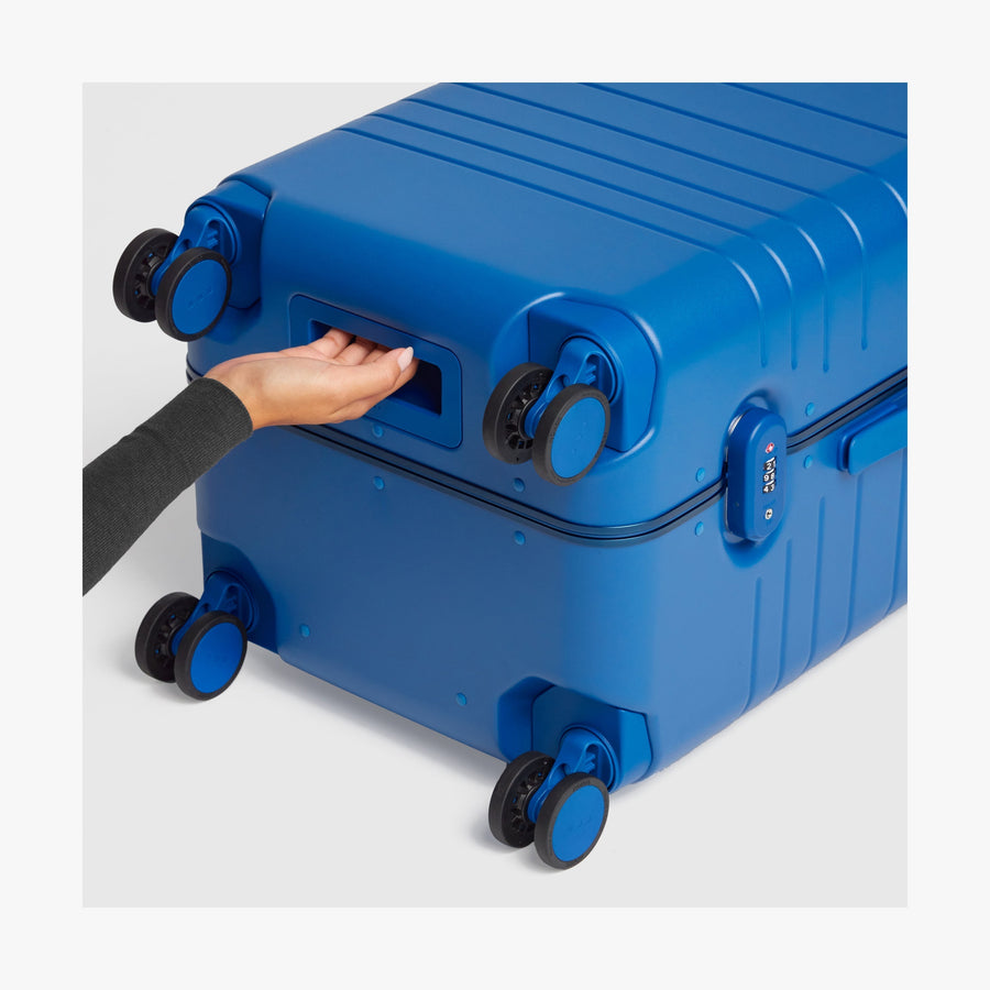 Coastal Blue | Close-up view of a hand gripping the built-in underside handle of a Coastal Blue Hybrid suitcase