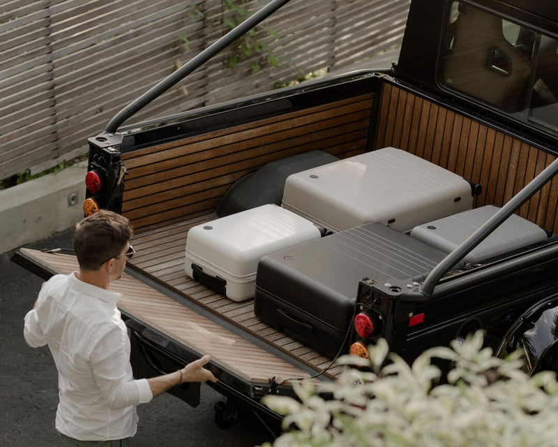 Man loading suitcases into a black truck bed with wooden floor.