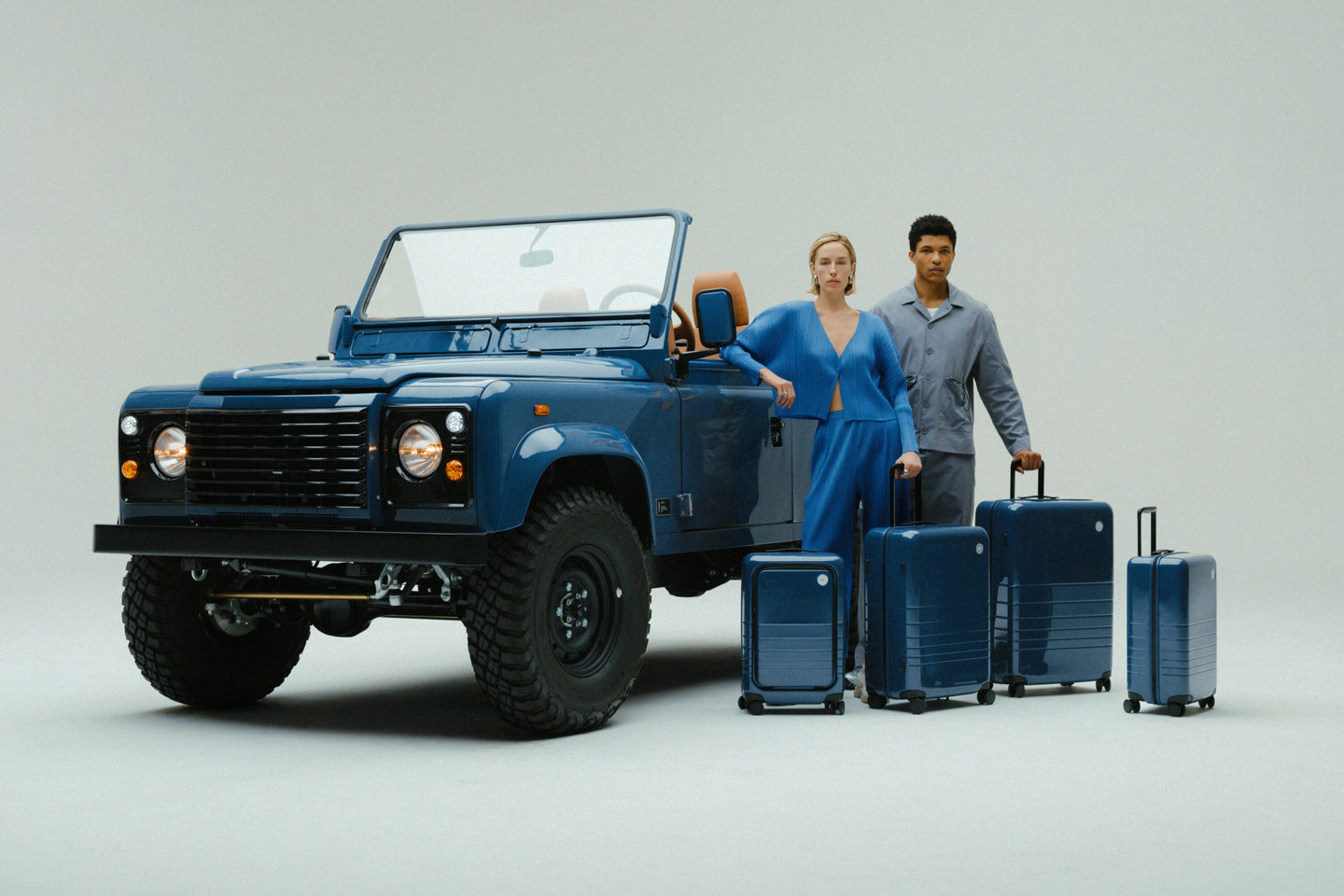 A woman and man stand beside the custom Arles Blue Land Rover Defender 90 with the full Arles Blue Glossy luggage collection.