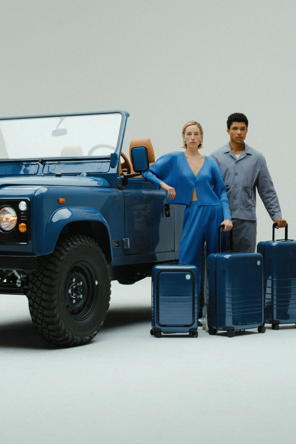 A woman and man stand beside the custom Arles Blue Land Rover Defender 90 with the full Arles Blue Glossy luggage collection.