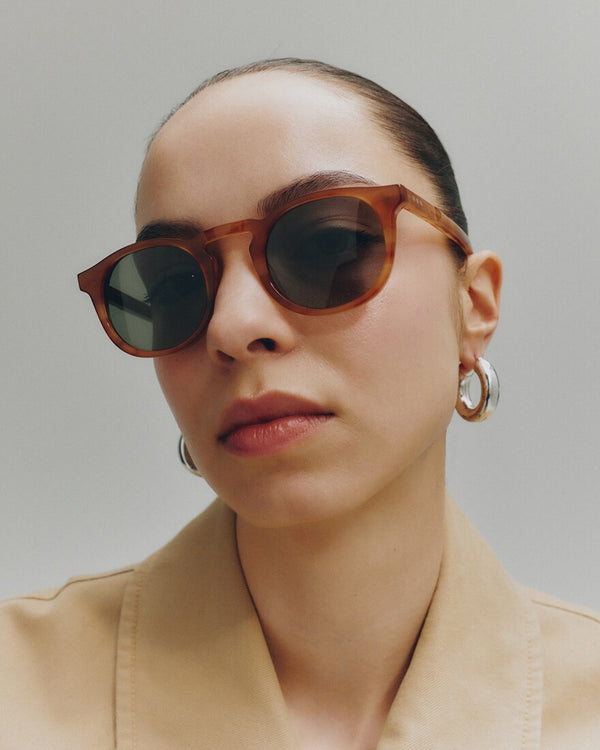 Person wearing round sunglasses with a neutral background