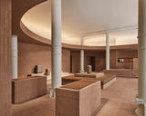 Wide interior of the Monos SoHo store featuring terracotta brick walls, white columns, and tiered seating with aluminum luggage displayed under a softly illuminated curved ceiling.