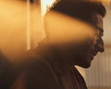 A close-up profile of Adrien Brody, partially obscured by golden sunlight streaming through a window, creating a warm and introspective atmosphere.